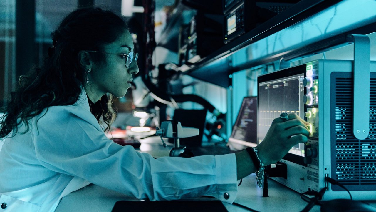 Una ricercatrice analizza circuiti elettronici utilizzando un oscilloscopio, valutando le prestazioni di schede elettroniche durante una fase di test in laboratorio.