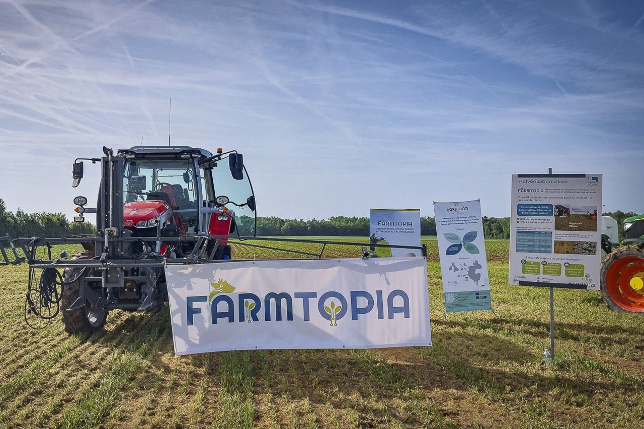 Trattore per l'irrorazione in un campo agricolo durante il secondo Open Day del SIP 8. A fianco del trattore si trovano cartelloni esplicativi del progetto