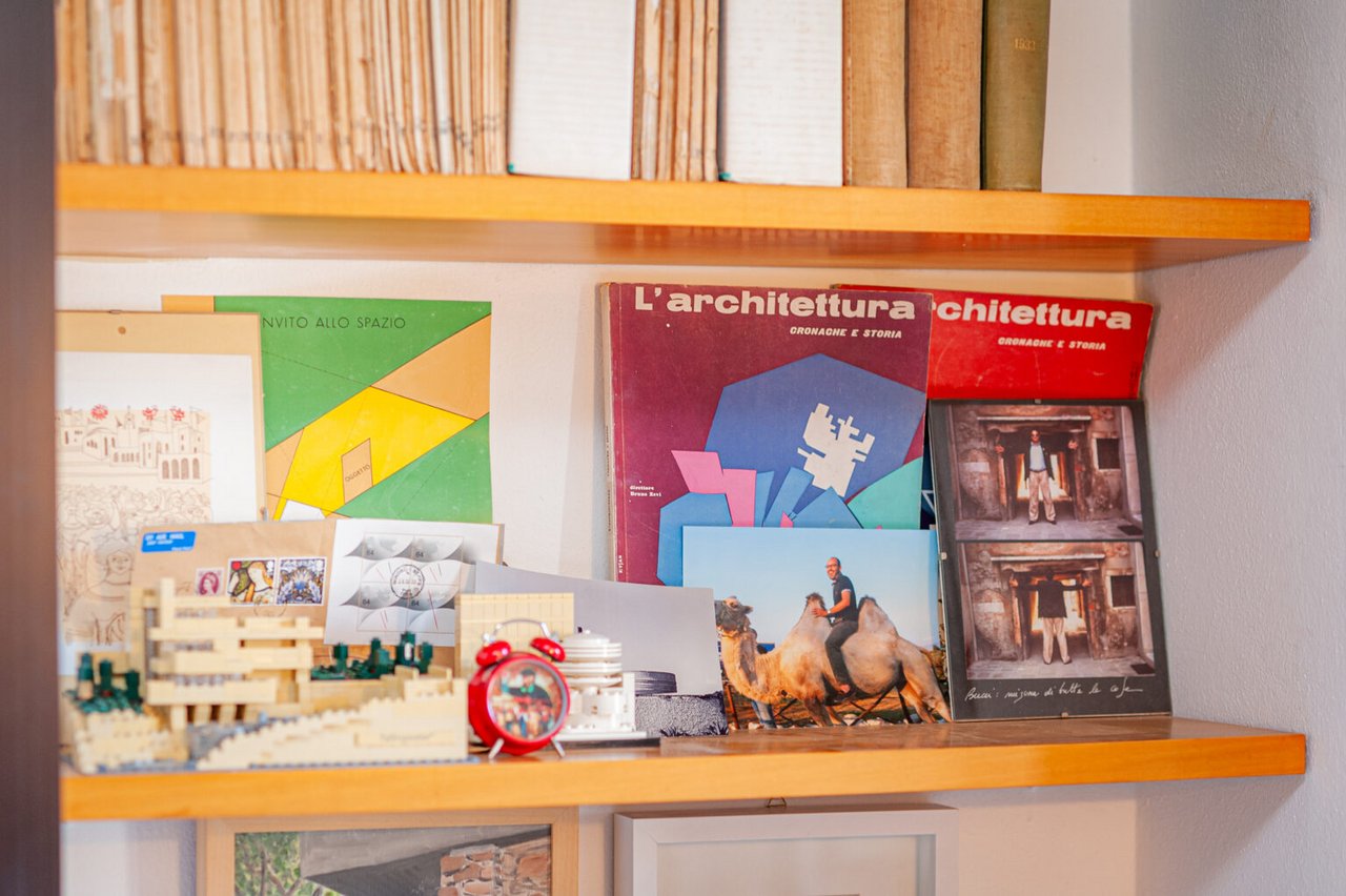 Scaffale con libri, riviste di architettura e varie stampe, che mostrano l'ambiente di ricerca di uno storico