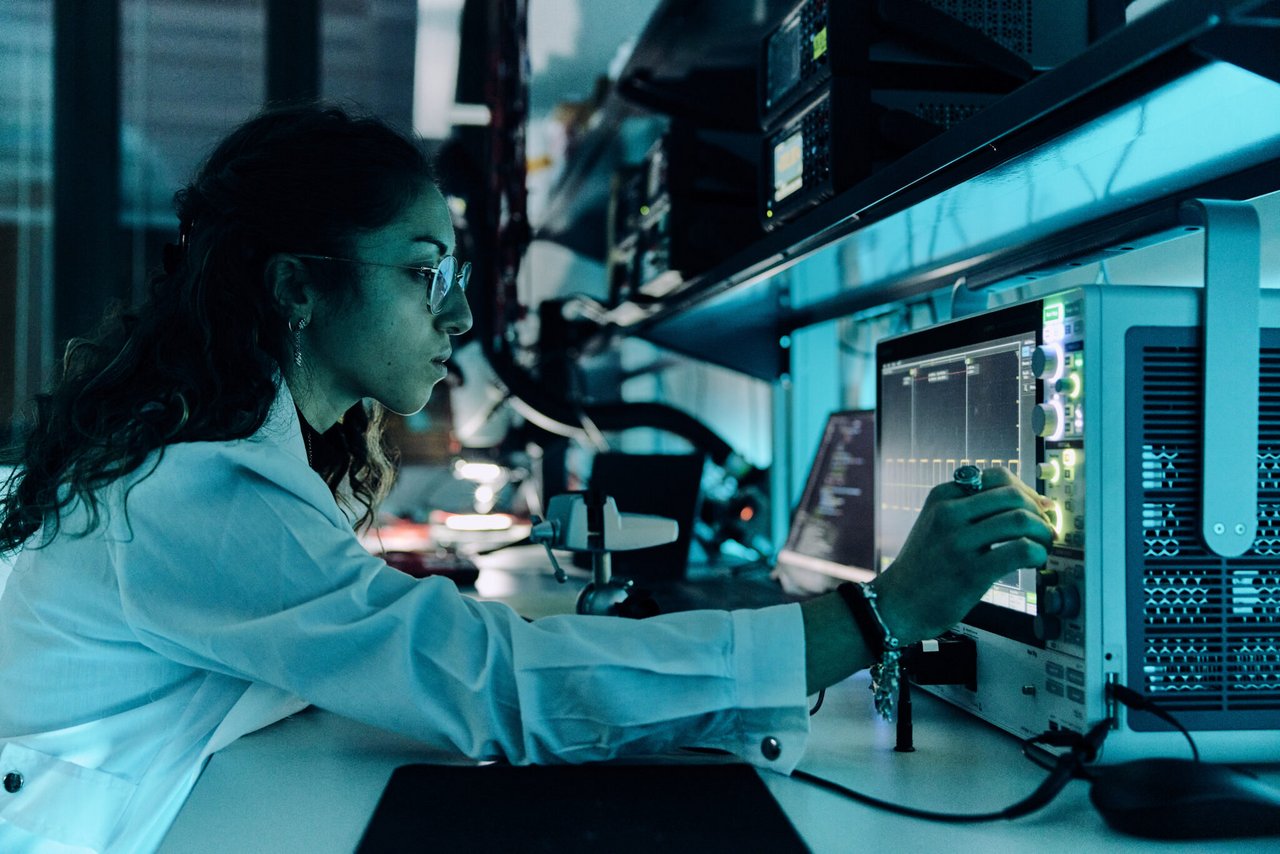 Una ricercatrice analizza circuiti elettronici utilizzando un oscilloscopio, valutando le prestazioni di schede elettroniche durante una fase di test in laboratorio.