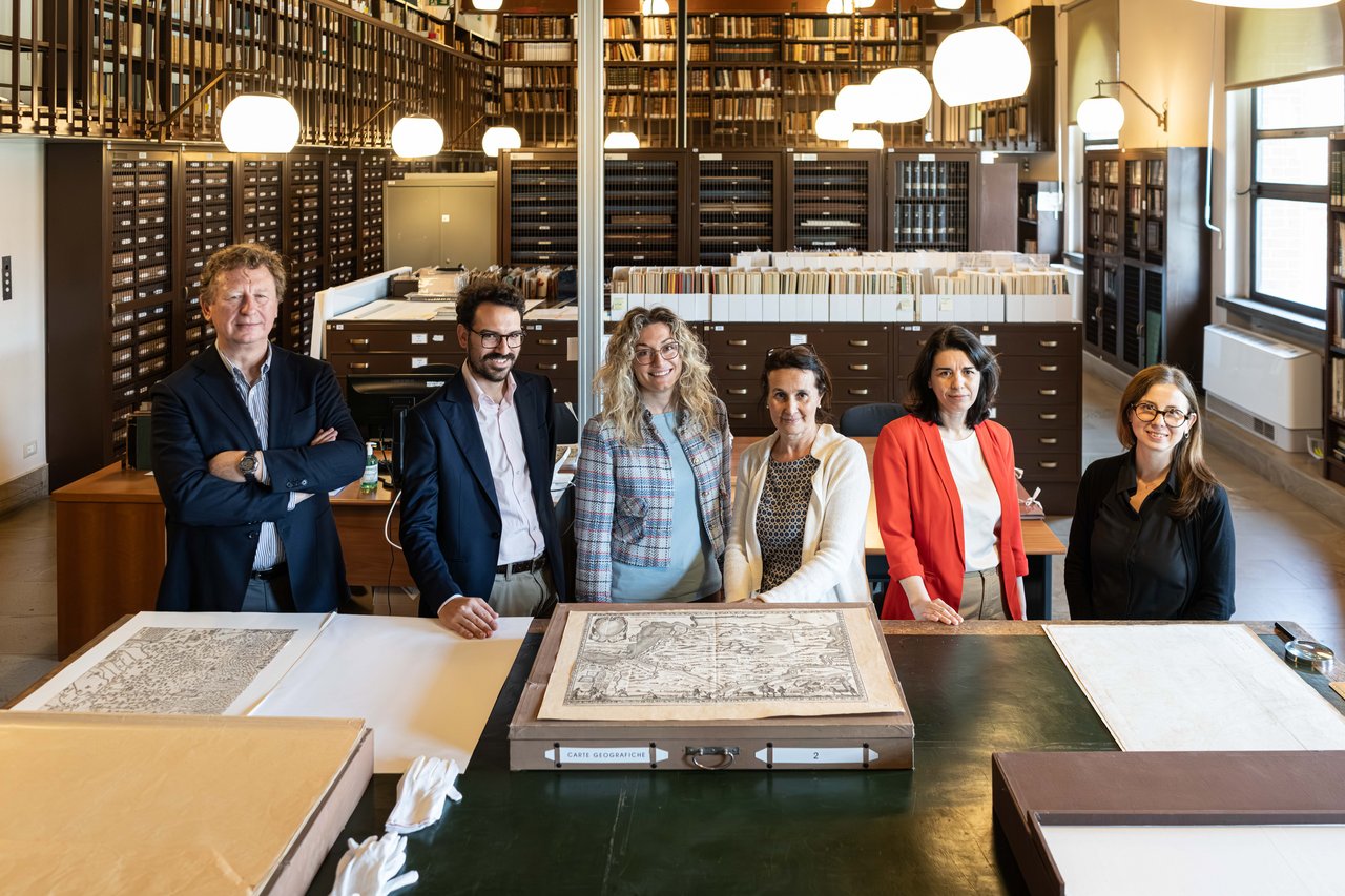 Research group in the room of the Civica Raccolta delle Stampe “Achille Bertarelli”, in front of a table with several historical maps.