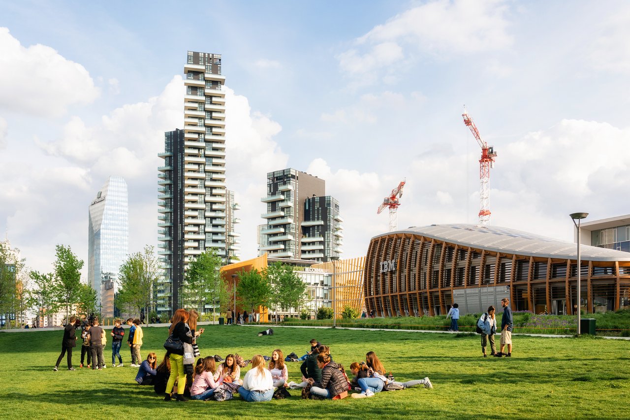 People relax on the lawn, with the skyscrapers of Piazza Gae Aulenti in the background, Milan.